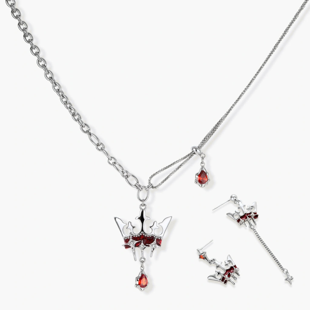 Silver-tone crown pendant with red zirconia stones and matching asymmetrical earrings on cream background