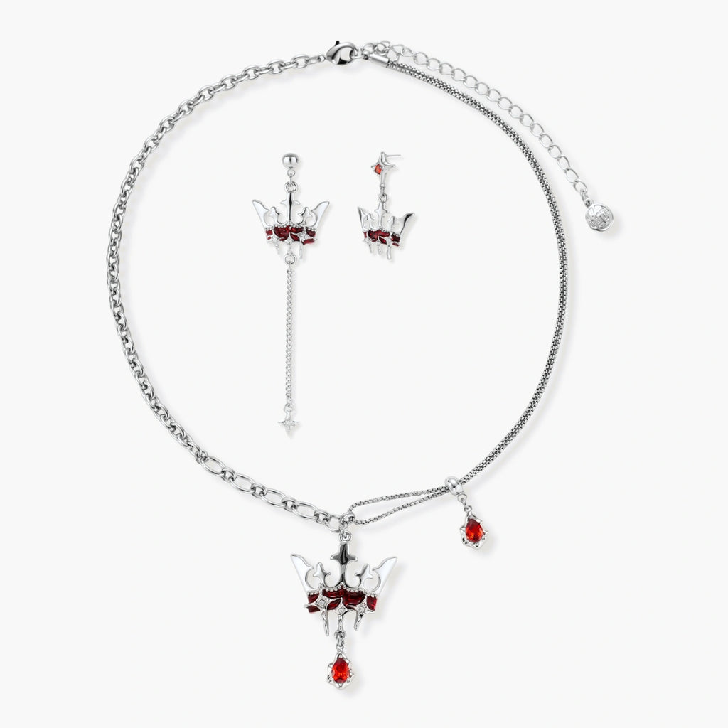 Silver-tone crown pendant with red zirconia stones and matching asymmetrical earrings on cream background
