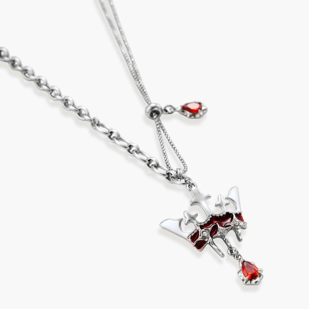 Silver-tone crown pendant with red zirconia stones and matching asymmetrical earrings on cream background