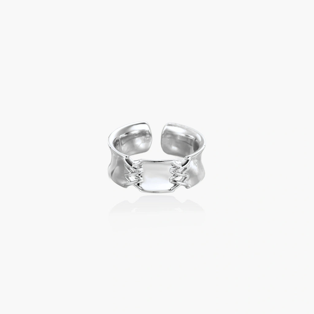 Adjustable silver-toned ring with sculptural stitch design across polished white gold-plated brass band