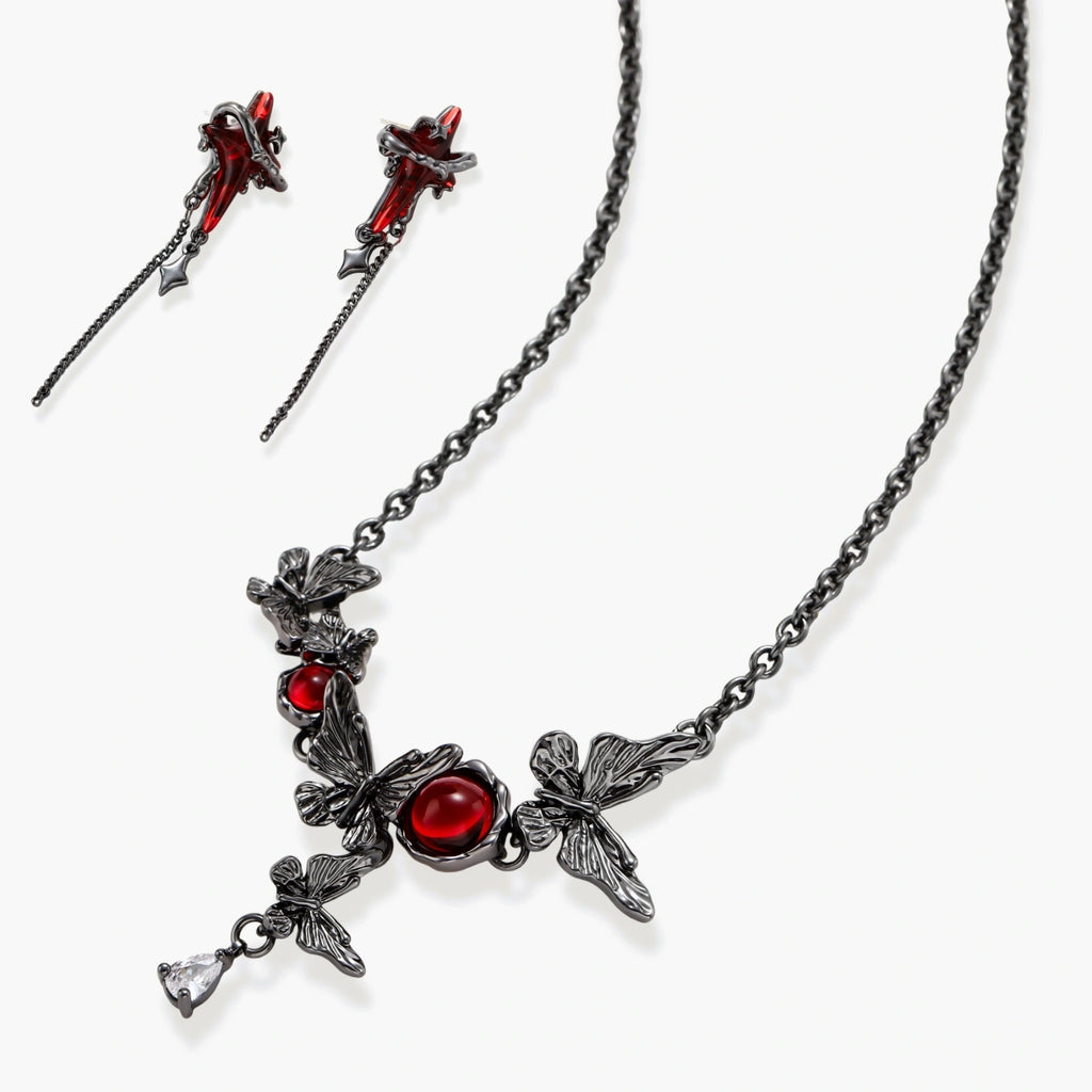 Gothic jewelry set with red resin cross pendants wrapped in dark metal chains on cream background.