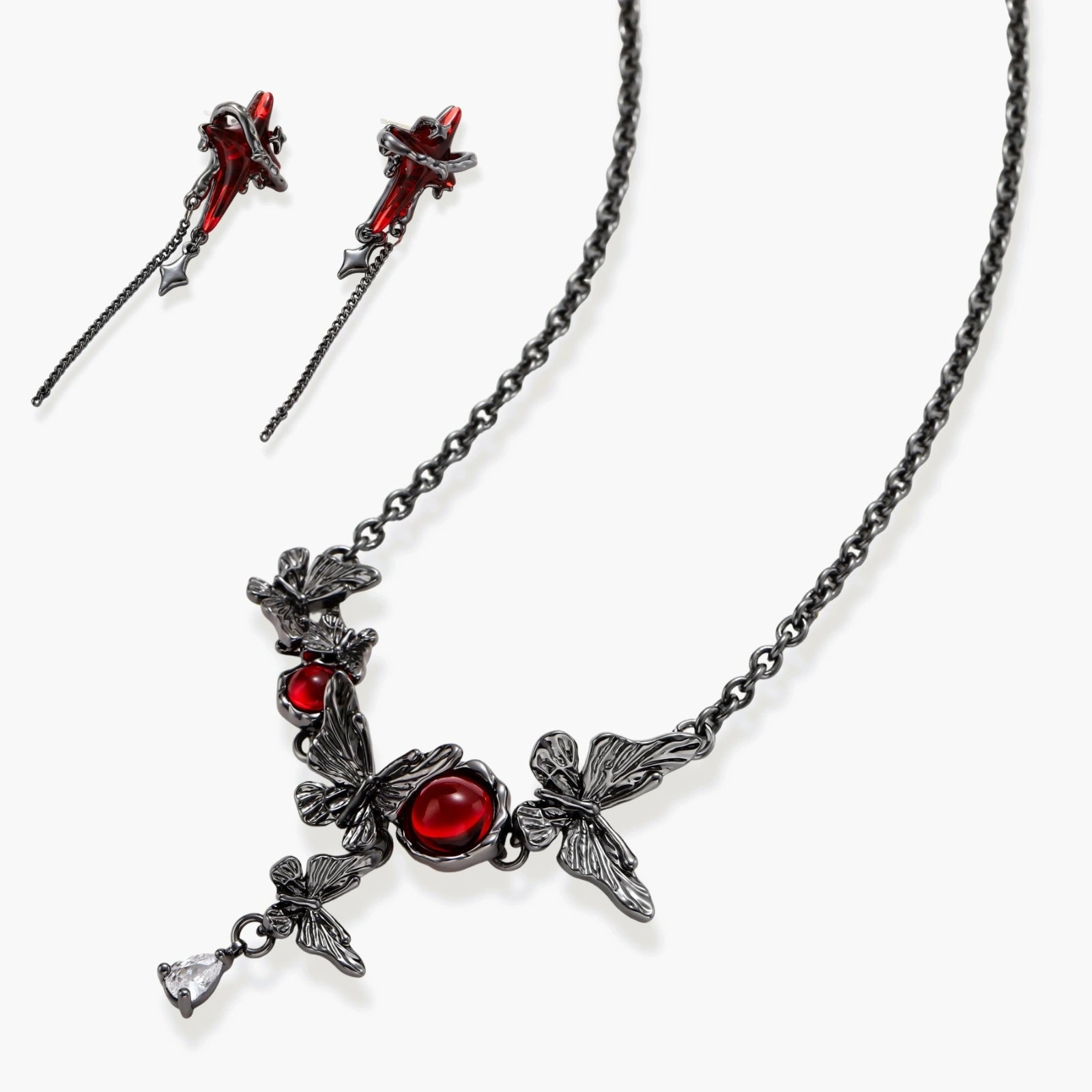 Gothic jewelry set with red resin cross pendants wrapped in dark metal chains on cream background.