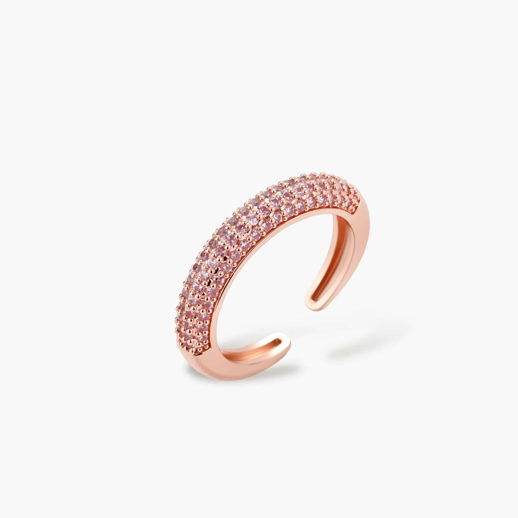 Rose gold jewelry set with pavé cubic zirconia stones including curved necklace, hoop earrings, and adjustable ring on cream background.